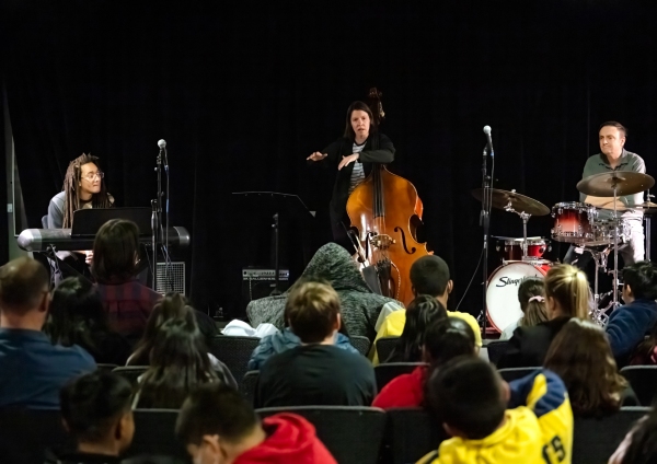 Bass player presenting at Jazz for the Schools, photo is taken facing stage over a sea of students.
