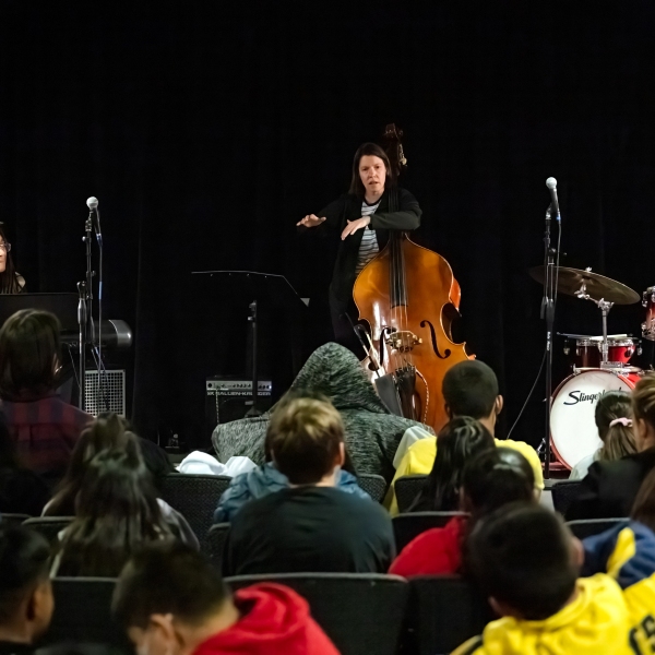 Bass player presenting at Jazz for the Schools, photo is taken facing stage over a sea of students.